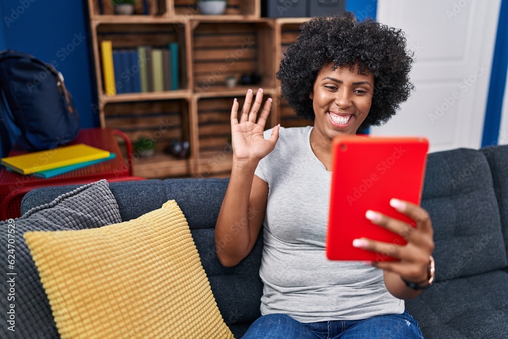 Black woman with curly hair using touchpad sitting on the sofa looking positive and happy standing and smiling with a confident smile showing teeth Black woman with curly hair using touchpad sitting on the sofa looking positive and happy standing and smiling with a confident smile showing teeth