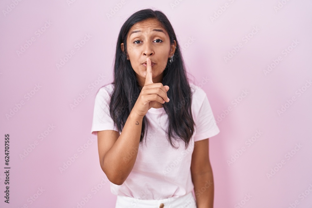 Young hispanic woman standing over pink background asking to be quiet with finger on lips. silence and secret concept. Young hispanic woman standing over pink background asking to be quiet with finger on lips. silence and secret concept.