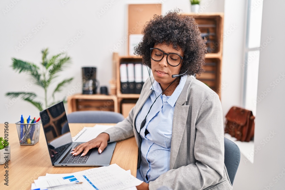 Black woman with curly hair wearing call center agent headset at the office looking sleepy and tired, exhausted for fatigue and hangover, lazy eyes in the morning.