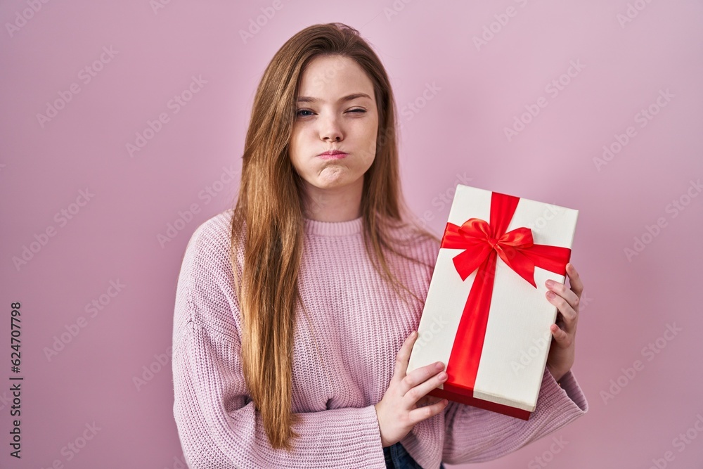 Young caucasian woman holding gift puffing cheeks with funny face. mouth inflated with air, catching air. Young caucasian woman holding gift puffing cheeks with funny face. mouth inflated with air, catching air.