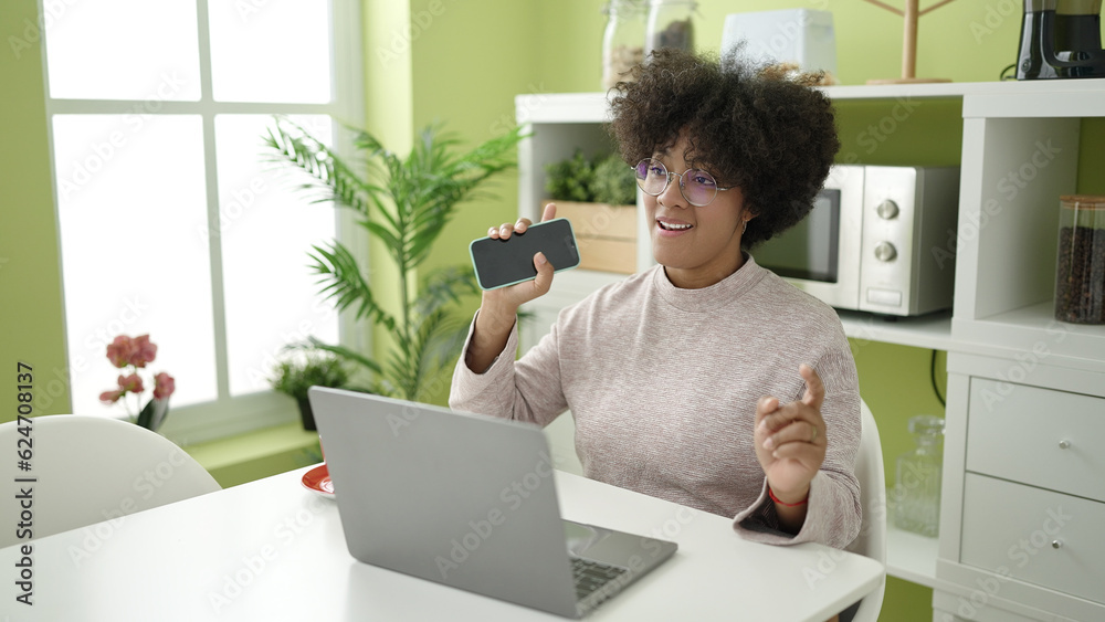 Young african american woman using laptop singing song using smartphone as a microphone at home