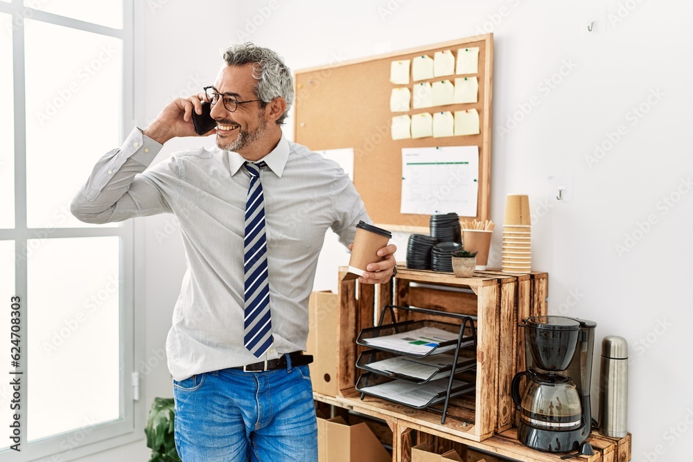 Middle age grey-haired man business worker talking on smartphone drinking coffee at office Middle age grey-haired man business worker talking on smartphone drinking coffee at office