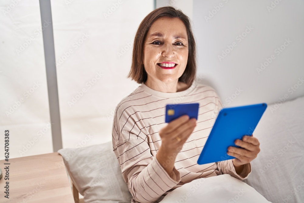 Middle age woman using touchpad and credit card sitting on bed at bedroom Middle age woman using touchpad and credit card sitting on bed at bedroom