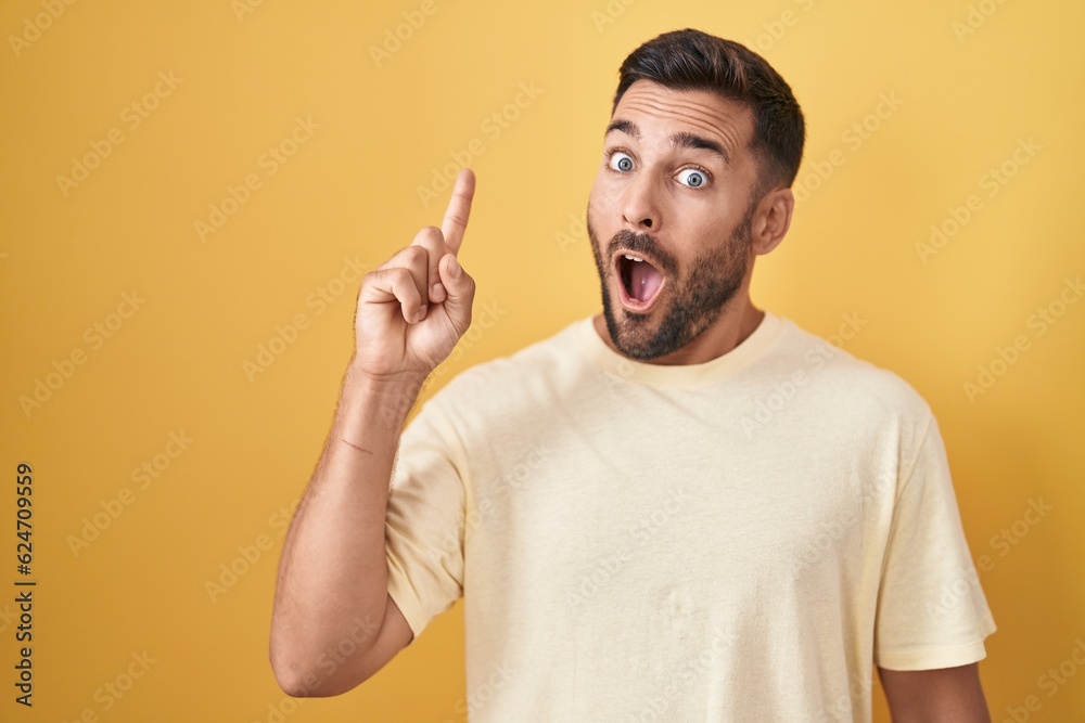 Handsome hispanic man standing over yellow background pointing finger up with successful idea. exited and happy. number one. Handsome hispanic man standing over yellow background pointing finger up with successful idea. exited and happy. number one.