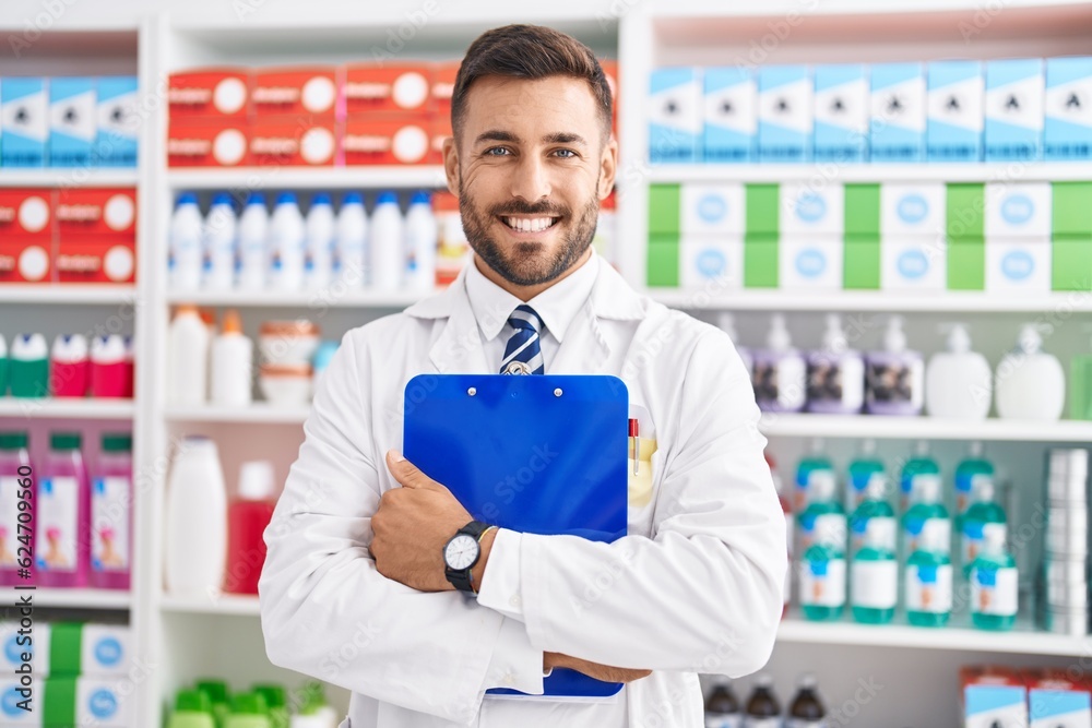 Young hispanic man pharmacist smiling confident holding clipboard at pharmacy