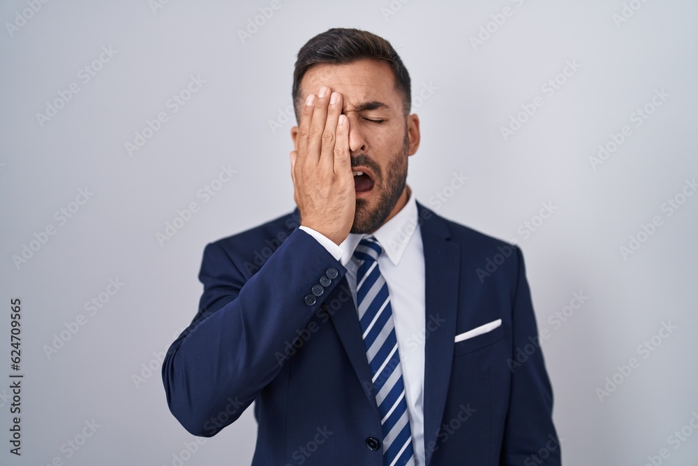 Handsome hispanic man wearing suit and tie yawning tired covering half face, eye and mouth with hand. face hurts in pain. Handsome hispanic man wearing suit and tie yawning tired covering half face, eye and mouth with hand. face hurts in pain.