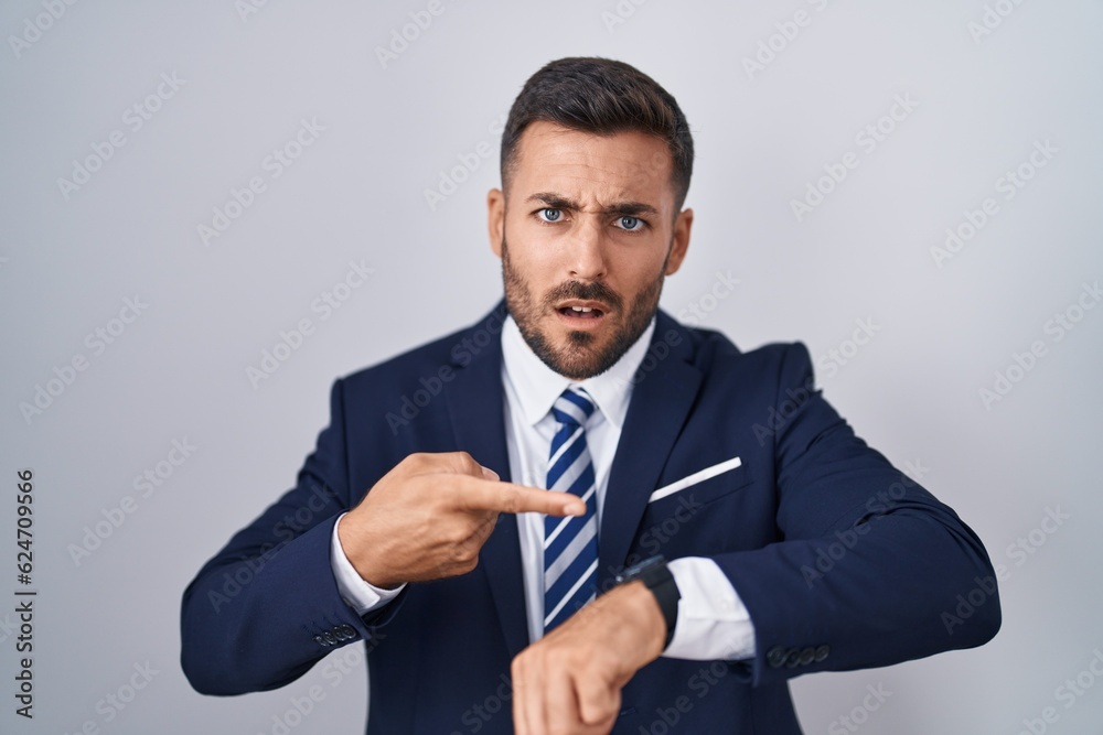 Handsome hispanic man wearing suit and tie in hurry pointing to watch time, impatience, upset and angry for deadline delay Handsome hispanic man wearing suit and tie in hurry pointing to watch time, impatience, upset and angry for deadline delay