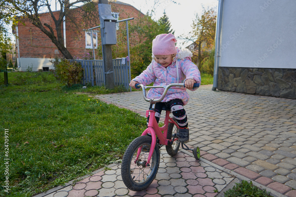 a little girl rides a bicycle in autumn,a child in a jacket rides a bicycle in the yard