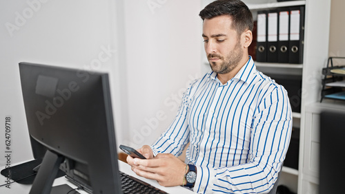 Young hispanic man business worker using smartphone with serious expression at office