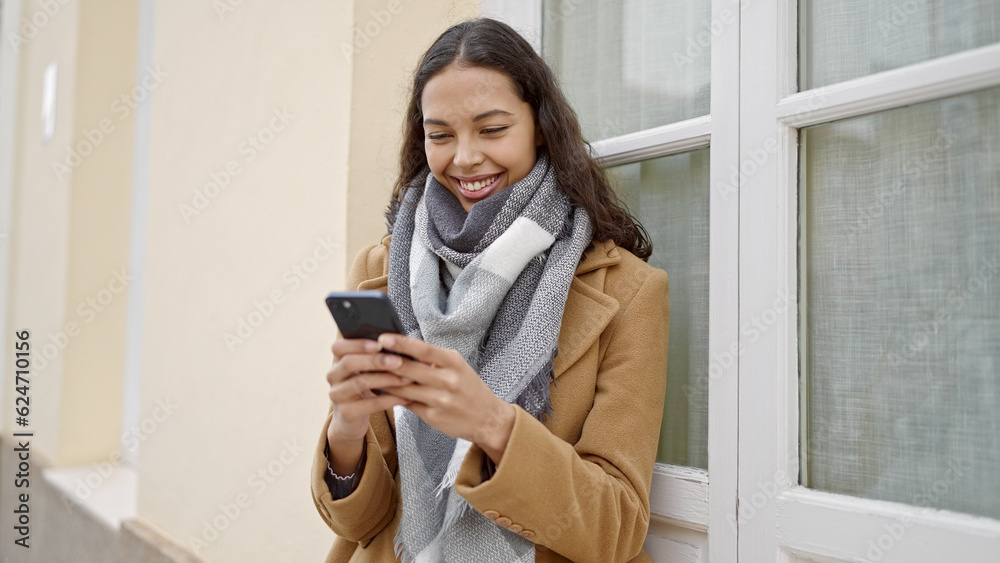Young beautiful hispanic woman using smartphone smiling at street