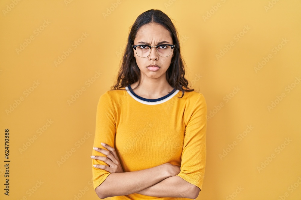 Obraz premium Young brazilian woman wearing glasses over yellow background skeptic and nervous, disapproving expression on face with crossed arms. negative person.