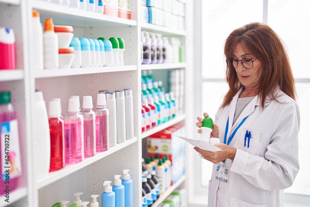 Middle age woman pharmacist holding bottle reading prescription at pharmacy