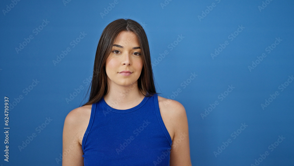 Young beautiful hispanic woman standing with serious expression over isolated blue background Young beautiful hispanic woman standing with serious expression over isolated blue background