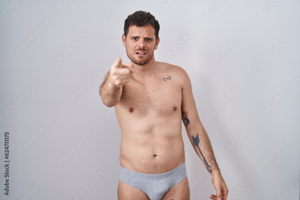Young hispanic man standing shirtless wearing underware pointing displeased and frustrated to the camera, angry and furious with you Young hispanic man standing shirtless wearing underware pointing displeased and frustrated to the camera, angry and furious with you