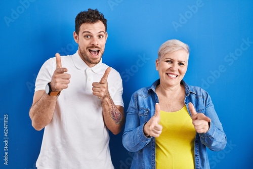 Young brazilian mother and son standing over blue background pointing fingers to camera with happy and funny face. good energy and vibes.