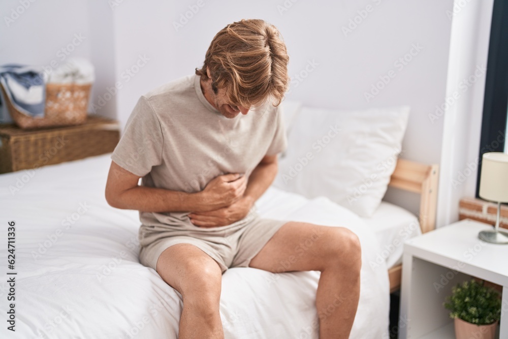 Young man suffering for stomach flu sitting on bed at bedroom Young man suffering for stomach flu sitting on bed at bedroom