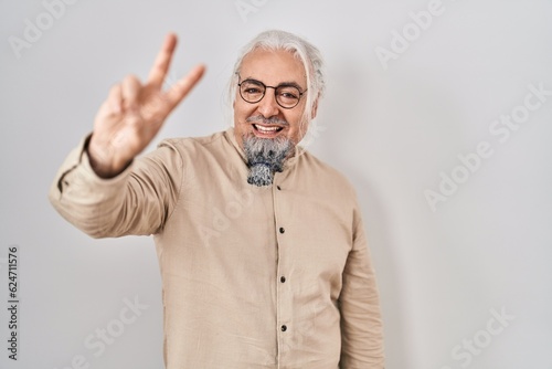 Middle age man with grey hair standing over isolated background smiling looking to the camera showing fingers doing victory sign. number two.