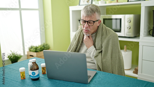 Middle age grey-haired man using laptop having online medical consultation at home