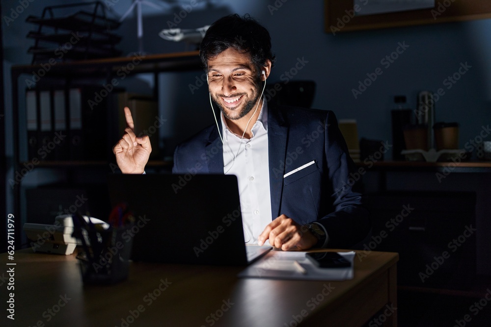 Handsome latin man working at the office at night pointing finger up with successful idea. exited and happy. number one. Handsome latin man working at the office at night pointing finger up with successful idea. exited and happy. number one.