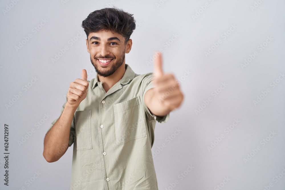 Arab man with beard standing over white background approving doing positive gesture with hand, thumbs up smiling and happy for success. winner gesture. Arab man with beard standing over white background approving doing positive gesture with hand, thumbs up smiling and happy for success. winner gesture.