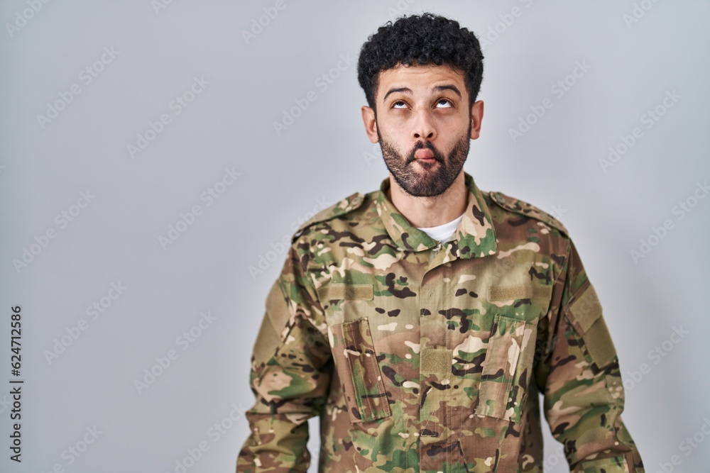 Arab man wearing camouflage army uniform making fish face with lips, crazy and comical gesture. funny expression. Arab man wearing camouflage army uniform making fish face with lips, crazy and comical gesture. funny expression.