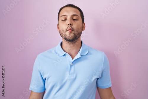 Hispanic man standing over pink background making fish face with lips, crazy and comical gesture. funny expression.
