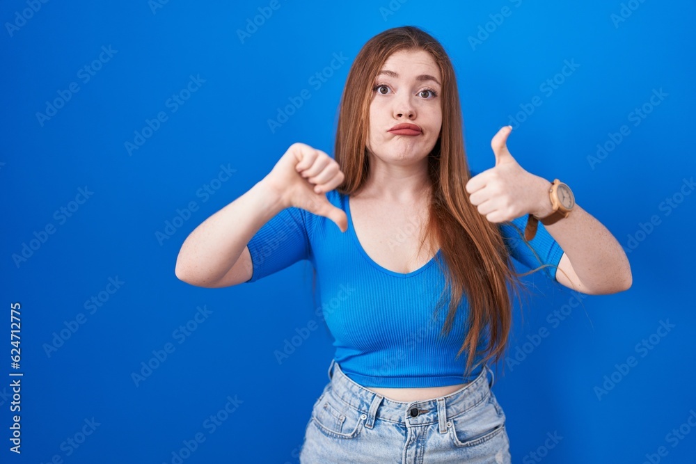 Redhead woman standing over blue background doing thumbs up and down, disagreement and agreement expression. crazy conflict Redhead woman standing over blue background doing thumbs up and down, disagreement and agreement expression. crazy conflict