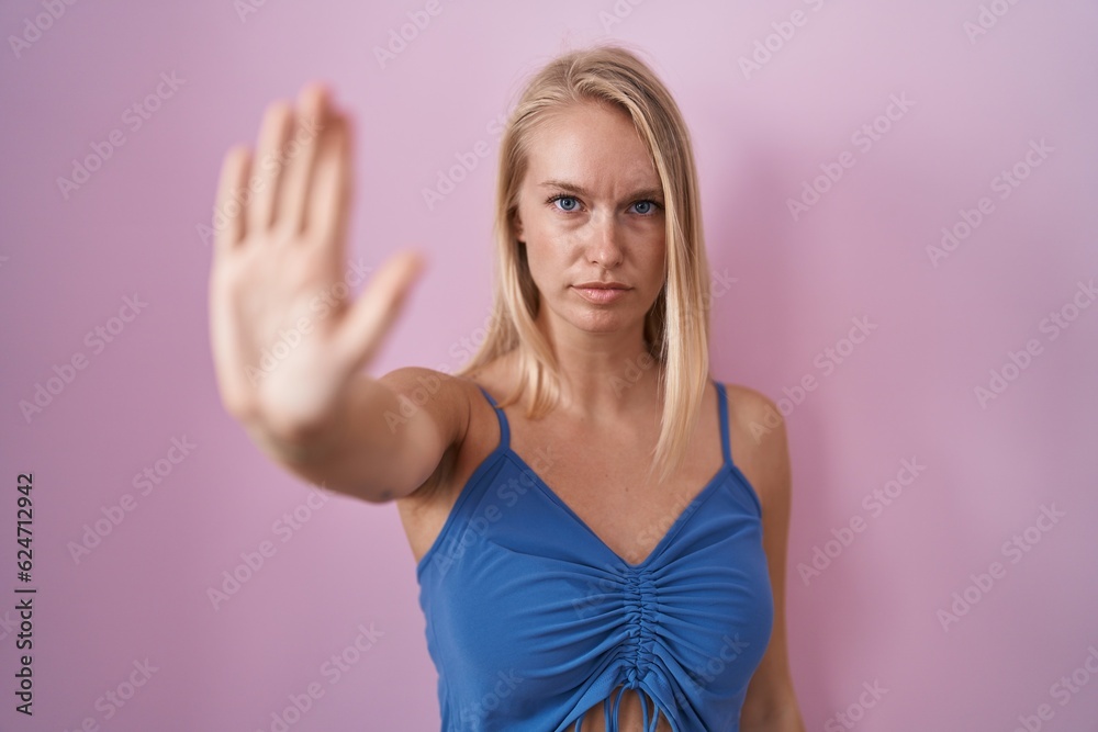 Young caucasian woman standing over pink background doing stop sing with palm of the hand. warning expression with negative and serious gesture on the face. Young caucasian woman standing over pink background doing stop sing with palm of the hand. warning expression with negative and serious gesture on the face.