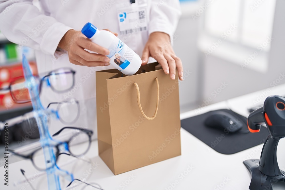 Young blonde woman pharmacist putting bottle on bag at pharmacy Young blonde woman pharmacist putting bottle on bag at pharmacy