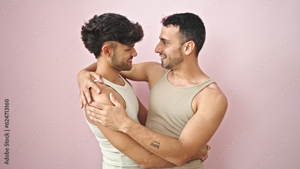 Two men couple smiling confident hugging each other over isolated pink background Two men couple smiling confident hugging each other over isolated pink background