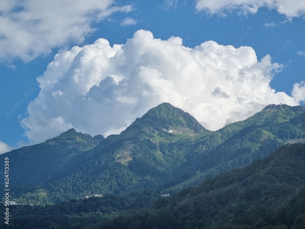 A solitary cloud drifts over the mountains, its fluffy form contrasting against the clear sky and creating a serene scene above the rugged peaks.