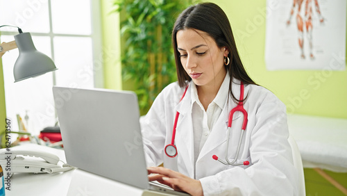 Young beautiful hispanic woman doctor using laptop working at clinic