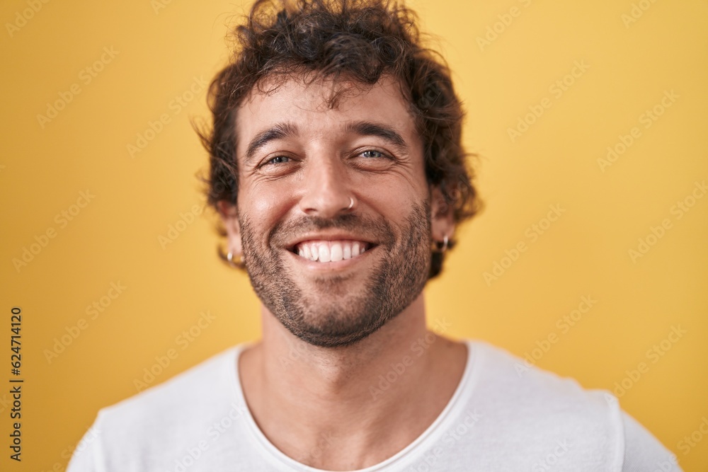 Obraz premium Young hispanic man smiling confident standing over isolated yellow background