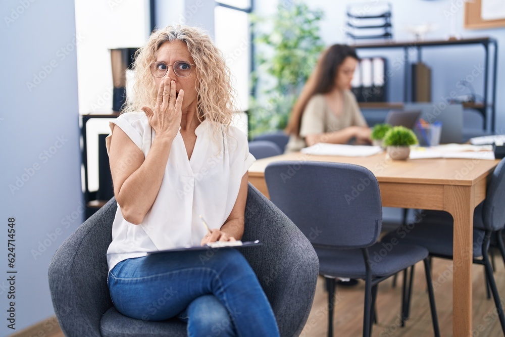 Middle age woman working at the office holding clipboard covering mouth with hand, shocked and afraid for mistake. surprised expression Middle age woman working at the office holding clipboard covering mouth with hand, shocked and afraid for mistake. surprised expression