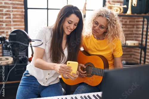Two women musicians playing classical guitar looking smartphone screen at music studio