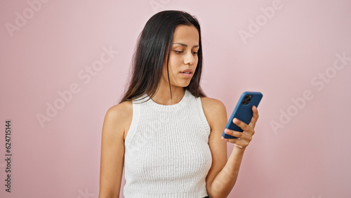Young beautiful hispanic woman using smartphone with serious expression over isolated pink background