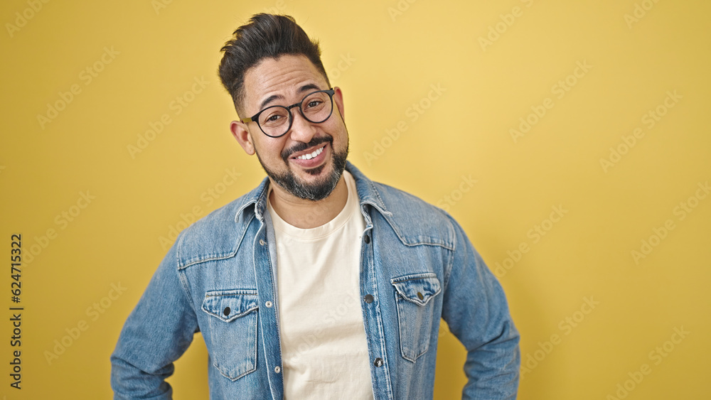 Young latin man smiling confident standing over isolated yellow background Young latin man smiling confident standing over isolated yellow background