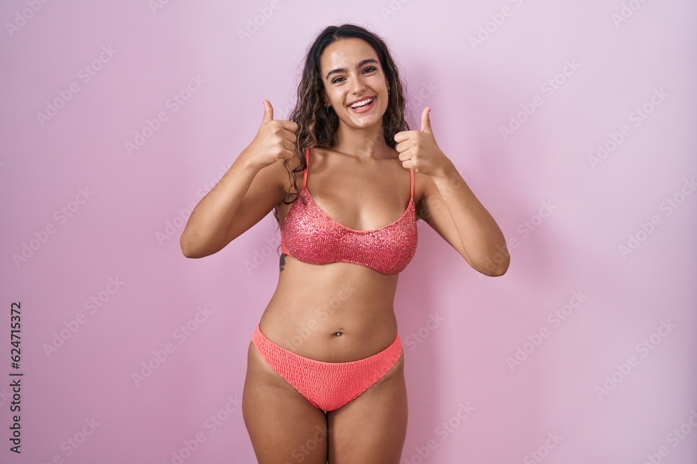 Young hispanic woman wearing lingerie over pink background success sign doing positive gesture with hand, thumbs up smiling and happy. cheerful expression and winner gesture. Young hispanic woman wearing lingerie over pink background success sign doing positive gesture with hand, thumbs up smiling and happy. cheerful expression and winner gesture.
