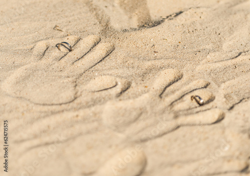 two hand prints with wedding rings on tropical sand beach, outdoor beach wedding concept