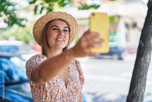 Young woman tourist wearing summer hat make selfie by smartphone at street