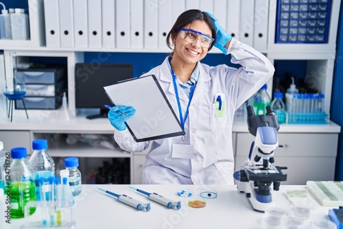 Hispanic young woman working at scientist laboratory smiling confident touching hair with hand up gesture  posing attractive and fashionable