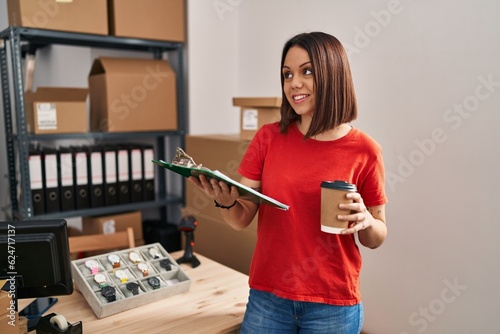 Young beautiful hispanic woman ecommerce business worker holding checklist drinking coffee at office