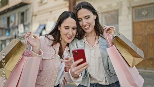 Two women going shopping holding bags using smartphone at street