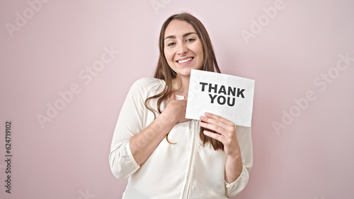 Young beautiful hispanic woman smiling confident holding thank you paper over isolated pink background
