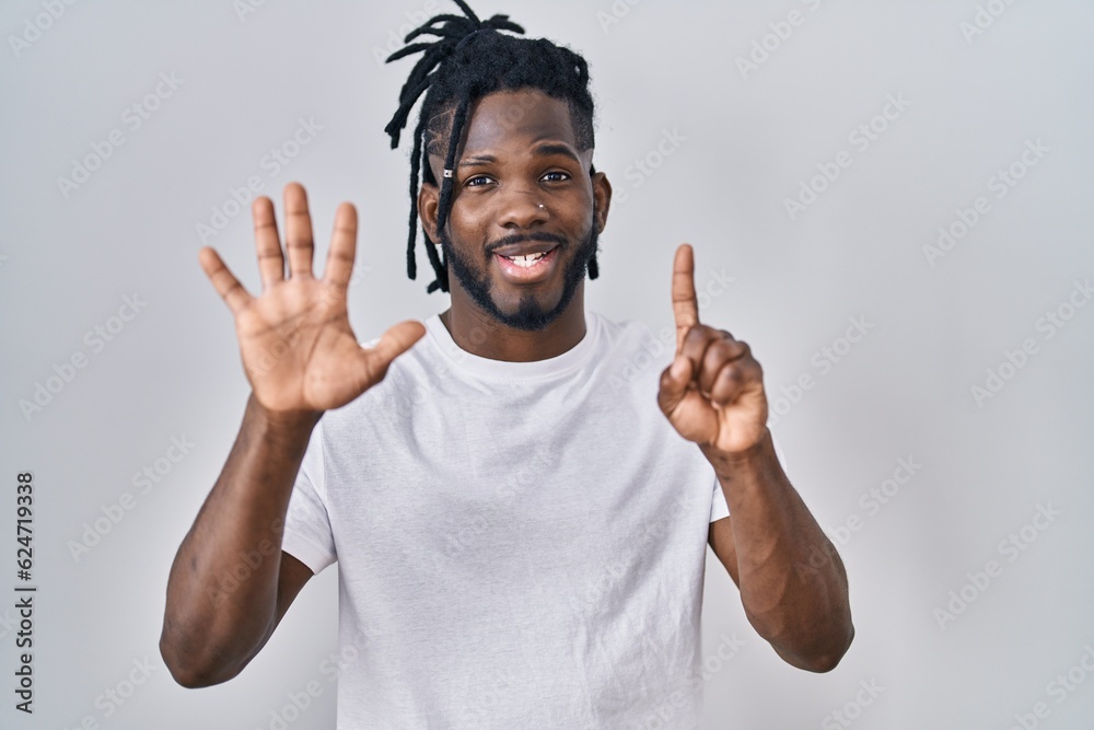 Fototapeta premium African man with dreadlocks wearing casual t shirt over white background showing and pointing up with fingers number six while smiling confident and happy.