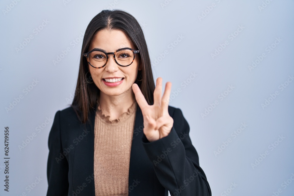 Young brunette woman standing over blue background showing and pointing up with fingers number three while smiling confident and happy. Young brunette woman standing over blue background showing and pointing up with fingers number three while smiling confident and happy.