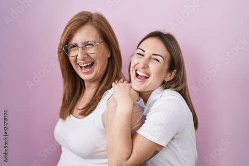 Hispanic mother and daughter wearing casual white t shirt smiling and laughing hard out loud because funny crazy joke.