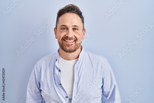 Middle age caucasian man standing over blue background with a happy and cool smile on face. lucky person.