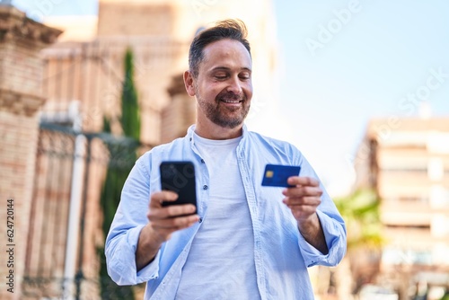 Young caucasian man using smartphone and credit card at street