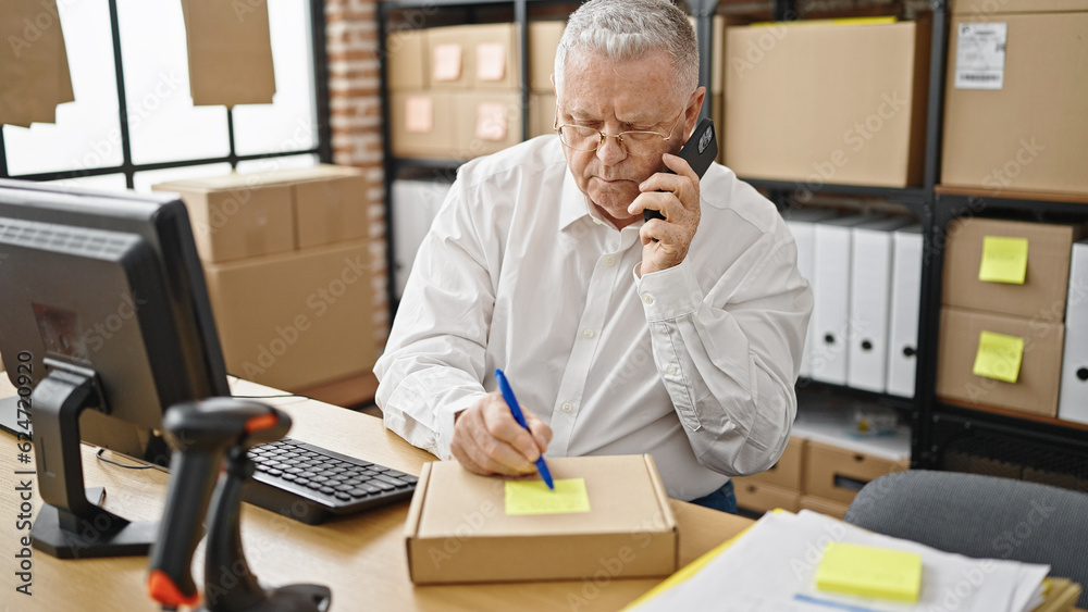 Middle age grey-haired man ecommerce business worker talking on smartphone writing on package at office Middle age grey-haired man ecommerce business worker talking on smartphone writing on package at office